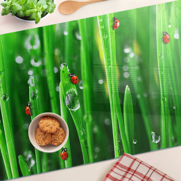 Planche à découper en verre Gouttes d'eau sur l'herbe avec des coccinelles